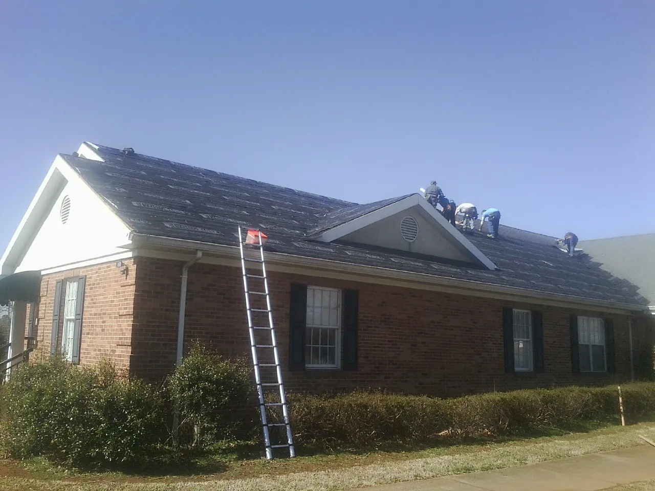 Crew tearing shingles off a brick ranch roof with a ladder set — Metal Roof Repair work by our crew in Ecru