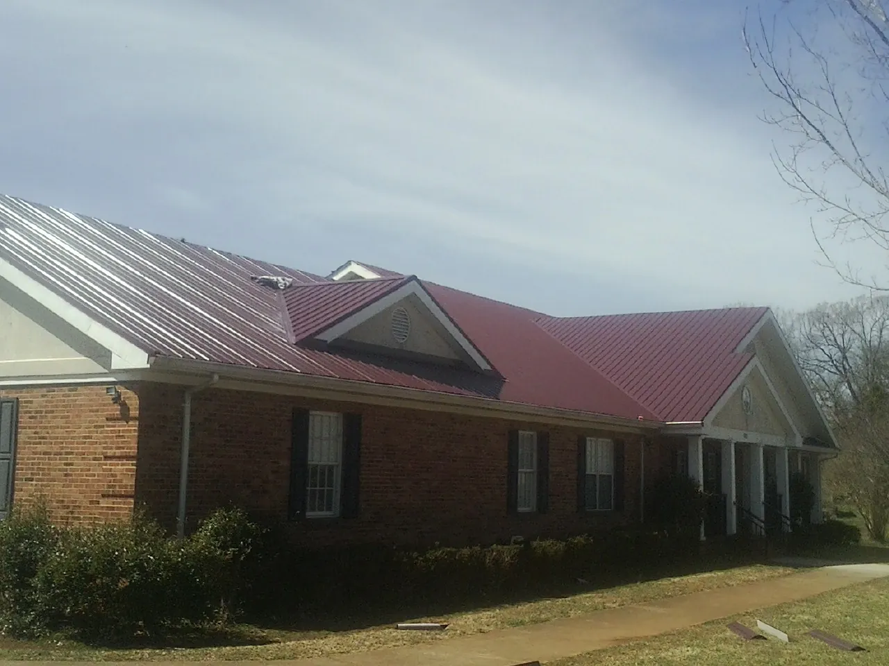 Red metal roof with gabled entries on a long brick building, from a Hail Damage Roof Repair job in Ecru