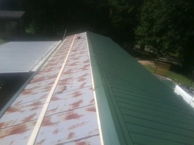 Old rusted panels beside newly installed green metal roofing — Wind Damage Roof Repair by Roofing Brothers in Ecru