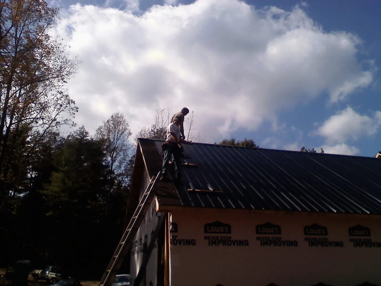 Roofer fastening dark metal panels high against a cloudy sky, from a Roof Inspection job in Ecru