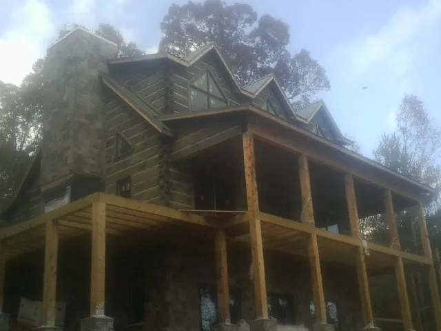 Stone chimney and dormers on a large log home with a timber porch in Ecru